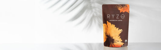 A picture of ryze mushroom coffee on a counter with plant leaves in the background.