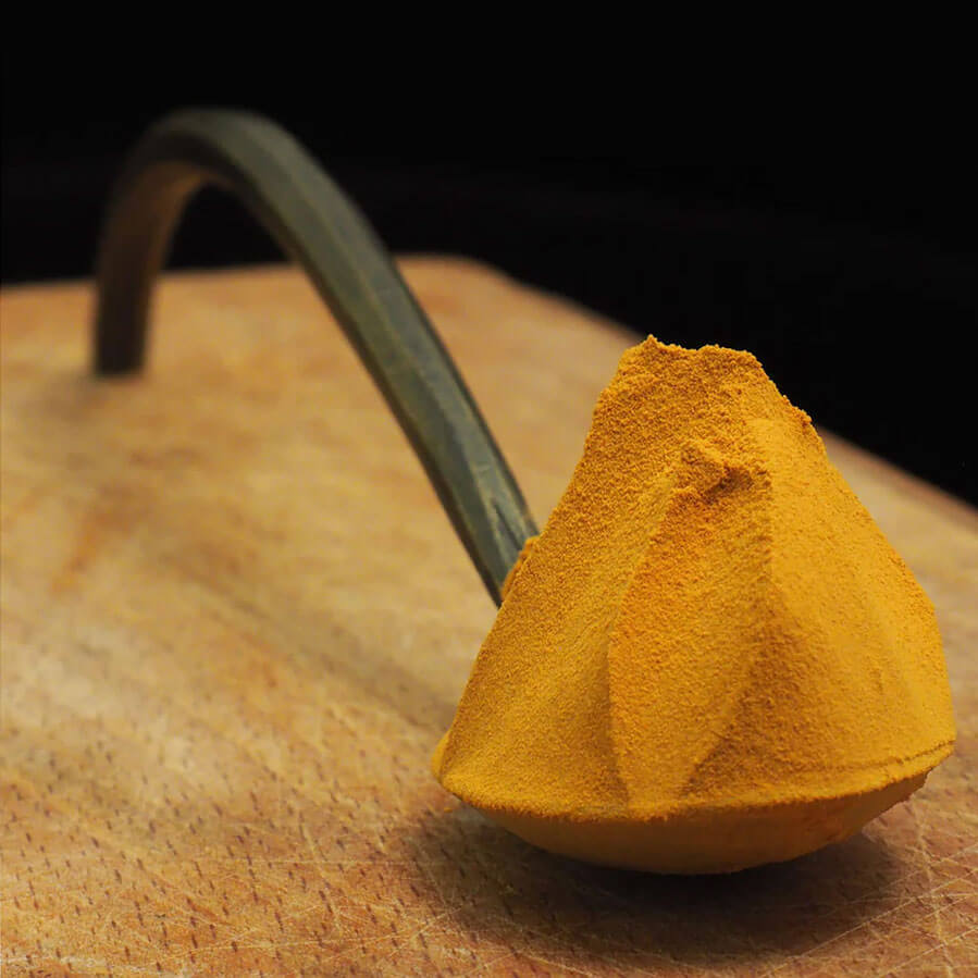 Golden mushroom extract powder on a metal spoon on a wooden table